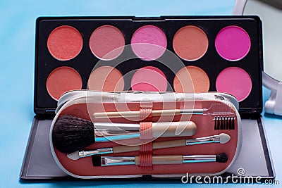 Cosmetic bag with brushes on a blue background, travel kit, flat palette with shadows and blushes, selective focus Stock Photo
