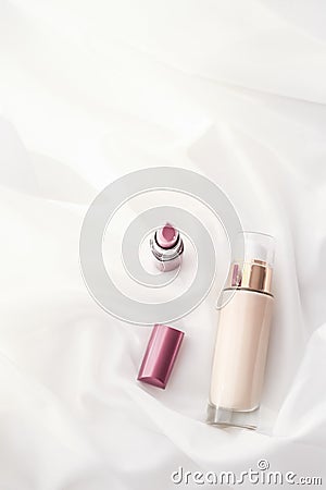 Beige tonal cream bottle make-up fluid foundation base and pink lipstick on silk background, cosmetics products as luxury beauty Stock Photo