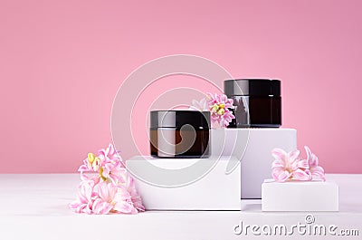 Cosmetic mockup - jars for cream of amber glass on white podiums with pink spring flowers. Template for branding identity. Stock Photo