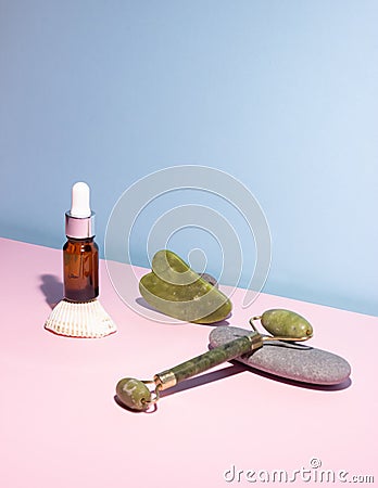 Cosmetic product in a glass bottle with a pipette and gua sha e scraper and roller. Smooth stones nearby. The concept of skin care Stock Photo