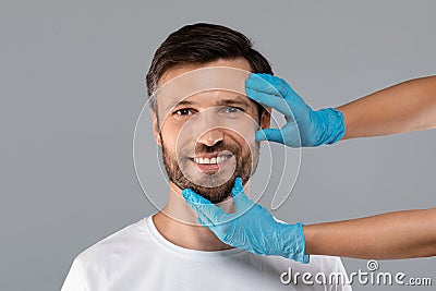 Cosmetician hands in protective gloves touching smiling man face Stock Photo