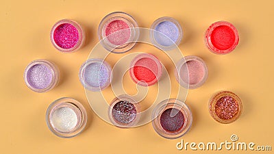 Cosmetics. Makeup. Jars with crumbly bright shadows, glitter. Pink,peach, golden colors on beige background. Closeup. Space for Stock Photo