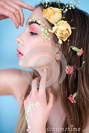 Cosmetics and manicure. Close-up portrait of attractive woman with dry flowers on her face and hair, pastel color, perfect make-up Stock Photo