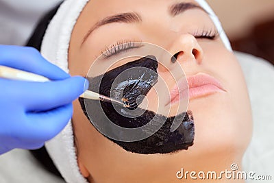 Cosmetologist does a black mask to cleanse the skin and anti-wrinkle on the face of a beautiful woman, spa treatments and Stock Photo