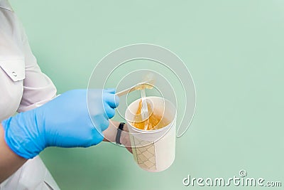 The cosmetologist holds a jar of sugar wax, shows texture of paste with a spatula Stock Photo
