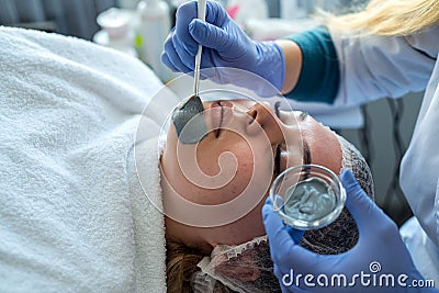 Cosmetologist makes dark mask on face young pretty woman in Spa salon Stock Photo