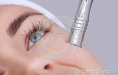 The cosmetologist makes the procedure Microdermabrasion of the facial skin of a beautiful, young woman in a beauty salon. Stock Photo