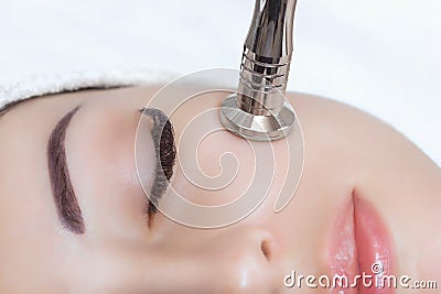 The cosmetologist makes the procedure Microdermabrasion of the facial skin of a beautiful, young woman Stock Photo