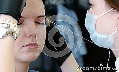 Cosmetologist performs the procedure of correction eyebrow threading. Side view. Stock Photo