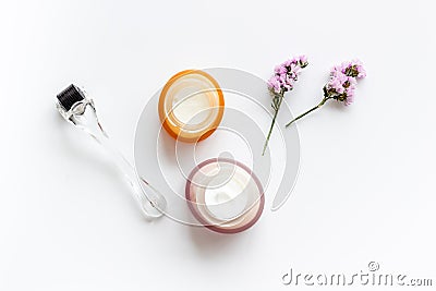 Cosmetologist tools. Dermaroller, creams near leaves and flowers on white background top-down Stock Photo