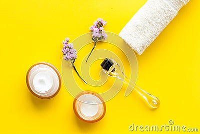 Cosmetologist tools. Dermaroller, creams near leaves and flowers on yellow background top-down flat lay Stock Photo