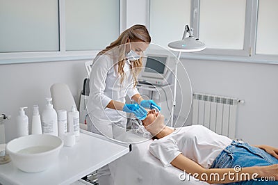 Cosmetologist using sponge to wash female face to prepare for cosmetic procedure Stock Photo