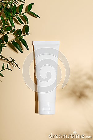 Cosmetology pink tube on minimalist beige background. Eye cream, foundation, concealer with green leaves on nude backdrop. Stock Photo