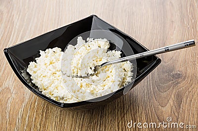 Cottage cheese and teaspoon in black bowl on table Stock Photo