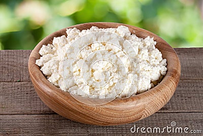 Cottage cheese in a wooden bowl on board with blurred garden background Stock Photo