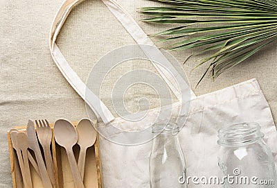 Cotton fabric tote bag wooden flatware cutlery crystal jar bottle green palm leaf on linen background. Plastic-free zero waste Stock Photo