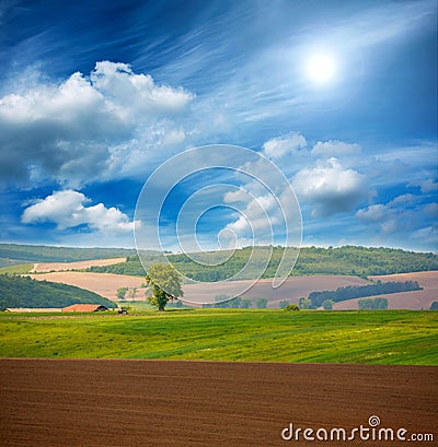 Country dry plowed earth agricultural green farmland on blue sky Stock Photo