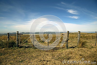 Country gate. Landscape of field and mountains. Nature. Blue sky with clouds. Grasslands Green. Outdoor. Access door. Chains. Moun Stock Photo