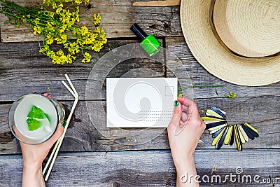 Countryside travel and vacation background. Female hands holding postcard surrounded with glass of lemonade, straw hat, wildflower Stock Photo