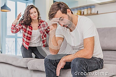 Couple argue. The wife shouted to her desperate husband, sitting on the couch in the living room at home. A man does not Stock Photo