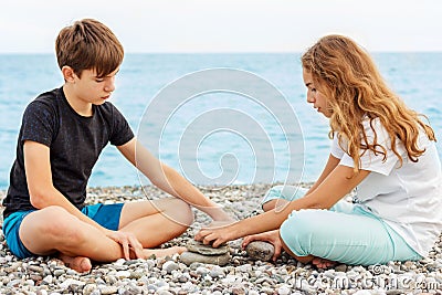 Couple of beautiful teens, first love. Girlfriend and boyfriend sitting on the beach and playing with pebble stones Stock Photo