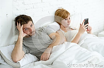 Couple in bed husband frustrated upset unsatisfied while wife using mobile phone Stock Photo