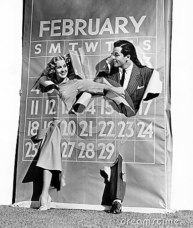 Couple bursting through leap year calendar Stock Photo