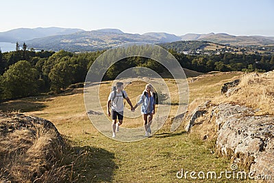 Couple Climbing Hill On Hike Through Countryside In Lake District UK Together Stock Photo