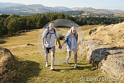 Couple Climbing Hill On Hike Through Countryside In Lake District UK Together Stock Photo