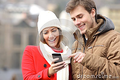 Couple consulting a smart phone in winter Stock Photo
