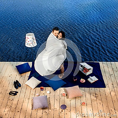 Couple covered by blanket standing on terrace near the water Stock Photo