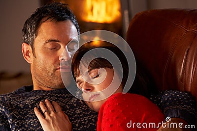 Couple Cuddling On Sofa By Cosy Log Fire Stock Photo