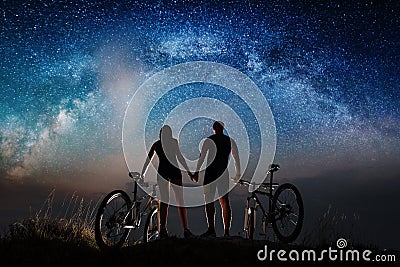 Couple cyclists with mountain bikes at night under starry sky Stock Photo