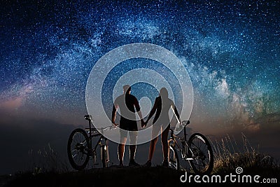 Couple cyclists with mountain bikes at night under starry sky Stock Photo