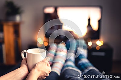 Couple drinking tea, hot chocolate, eggnog or mulled wine and watching tv in warm cozy woolen socks in winter. Stock Photo