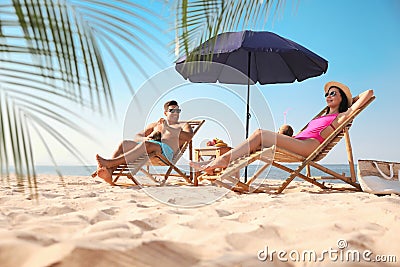 Couple with drinks resting on beach at resort Stock Photo