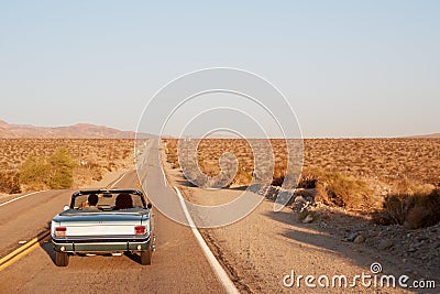 Couple driving convertible car on desert highway, back view Stock Photo