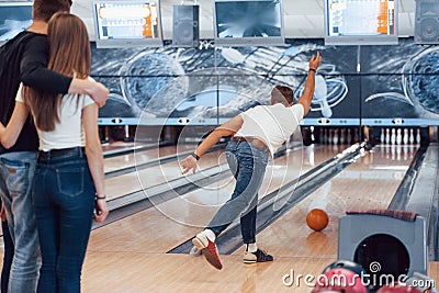 Couple embracing behind the man. Young cheerful friends have fun in bowling club at their weekends Stock Photo