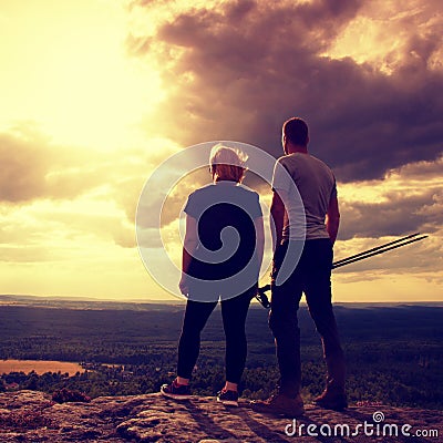 Couple enjoying marvellous moments during sunset . Young pair of hikers on the peak of rock watch over valley to Sun. Stock Photo