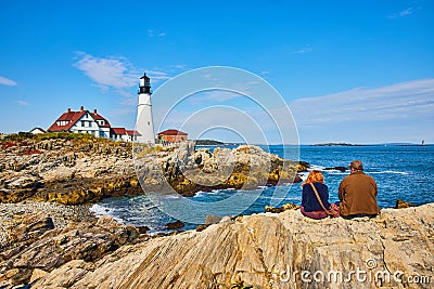 Couple enjoys view of lighthouse on Maine coastline sitting on rocks Editorial Stock Photo