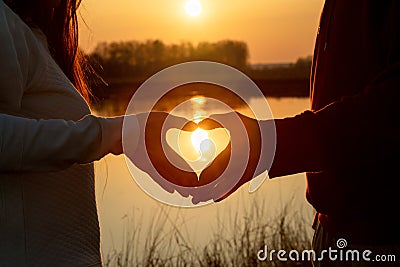 A couple gesturing hands shows a heart on the background of a sunny sunset Stock Photo