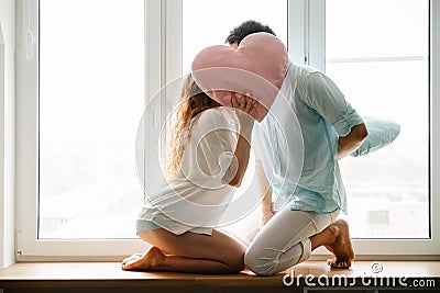 Couple girl and guy play with pillows near window. Stock Photo