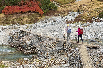 Couple Of Girls Are Hiking By Crossing The Bridge Over A Mountain River Editorial Stock Photo