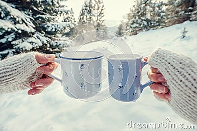 Couple hands in mittens take a mugs with hot tea in winter fores Stock Photo