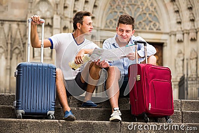 Couple of male tourists with baggage sitting with map at stairs Stock Photo