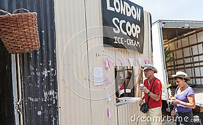 Couple in hats buying ice-cream from window opening in corrugated iron wall Editorial Stock Photo