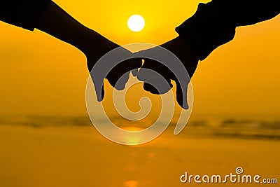 Couple holding each other hands using little pinky finger in background of sunrise at the beach Stock Photo