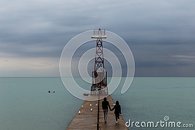 Couple holding hands walking along concrete pier jetty along Lake Michigan Stock Photo