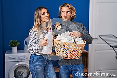 Couple holding laundry basket and detergent bottle smiling looking to the side and staring away thinking Stock Photo