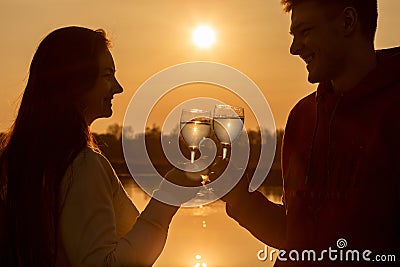 A couple holds glasses with drinks against the backdrop of a sunny sunset Stock Photo